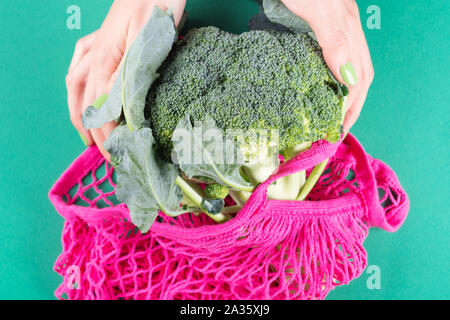 Null Abfall Konzept. Woman's Händen grüne Maniküre holding Rosa wiederverwendbare Tasche mit Brokkoli. Kunststoff freien Lebensstil Stockfoto