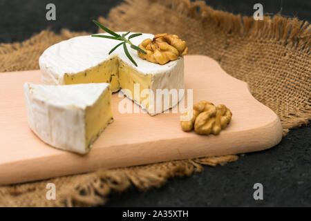 Camembert mit grünen garniert mit einem Zweig Rosmarin und Walnuss auf ein Holzbrett. Stockfoto
