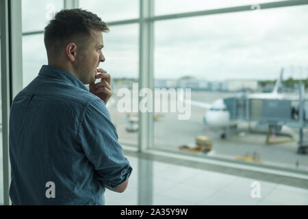 Kaukasischen jungen Mann Angst zu Flug stehen in Terminal in der Nähe der Fenster Stockfoto