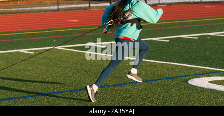 Ein High School Mädchen zieht eine gewichtete Schlitten auf grünem Rasen Feld während der Leichtathletik Geschwindigkeit Praxis. Stockfoto