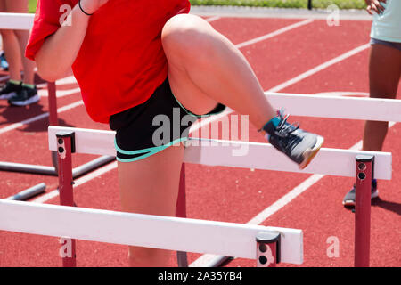 Ein High School Leichtathlet an der Praxis über Hürden auf einer roten Piste über den Sommer zu gehen. Stockfoto