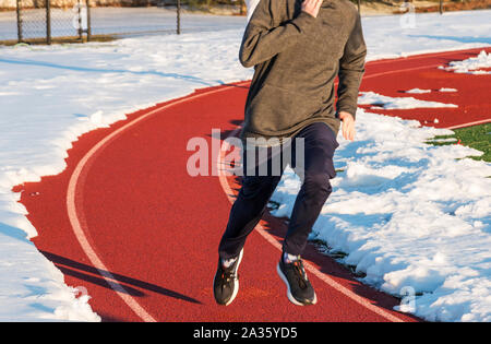 Ein High School Boy läuft auf einer Schiene in der Spur eines mit der restlichen Strecke mit Schnee im winter Leichtathletik Praxis abgedeckt. Stockfoto