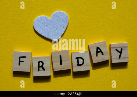 Freitag im Holz- Alphabet Buchstaben auf einem gelben Hintergrund mit einem weißen Glitter Herz Stockfoto