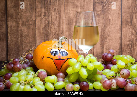 Glas Weißwein mit Kürbis und Weintrauben im Herbst. Imit einer natürlichen Holz- Platte als Hintergrund. Stockfoto