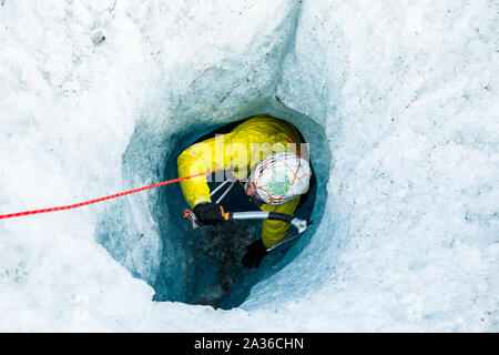 Man Klettern bis aus einem tiefen Loch gerade nach unten in das Eis des Salmon Glacier. Diese vertikale Eishöhle oder Moulin war von Wasser in den Gletscher. Stockfoto