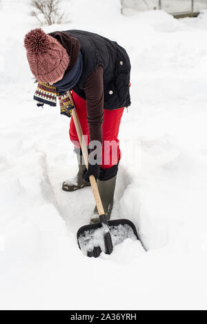 Frau in warme Kleidung mit schwarzem Kunststoff Schaufel mit Holzstiel macht der Pfad im Schnee. Close-up. Stockfoto