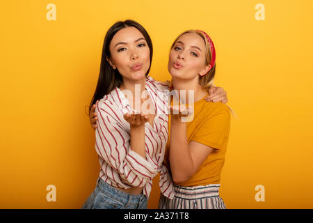 Zwei Mädchen senden Kuss zu sozialen Freunde. Emotionale und freudigen Ausdruck. Gelber Hintergrund Stockfoto