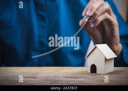 Eigenschaft Wachstum Konzept. Ein Geschäftsmann schreiben steigende Graph mit einem kleinen Haus Modell auf Holz Tisch. Stockfoto