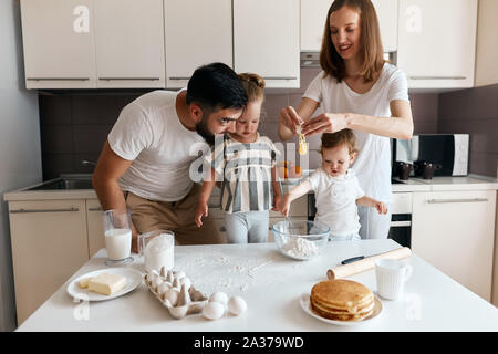 Junge fröhliche Frau und ihrer Familie, Kinder Teig, Aufschlagen der Eier zur Unterhaltung Konzept einfügen. Stockfoto