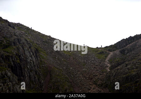 Menschen zu Fuß auf den Weg in die Scharte zwischen Breiten Felsen und die höchsten Wainwright Scafell Pike, Nationalpark Lake District, Cumbria, England, UK. Stockfoto