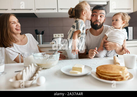 Lustige kleine Mädchen lecken Gesicht ihr Papa, während ihre Eltern helfen beim Kochen in der Küche. nach oben schließen Foto Stockfoto