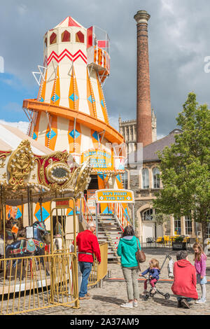 Ein Helter Skelter messe Fahrt auf Anker Square im Stadtzentrum von Bristol mit Rowes Leadworks Schornstein an der Rückseite, Avon, England, UK. Stockfoto