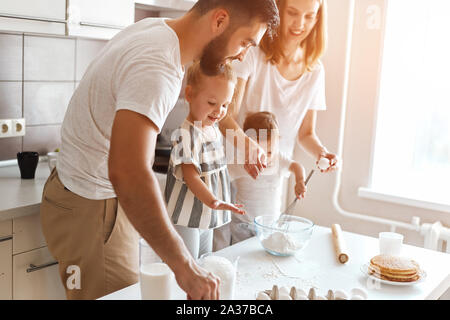 Junge fröhliche Paare und ihre Kinder versuchen, Kuchen zu kochen. Nahaufnahme Seite Foto anzeigen Stockfoto