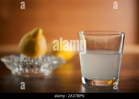 Frisch gepressten Zitronensaft in ein Trinkglas auf dem Küchentisch Platte mit halbierten Zitronen und Zitronenpresse in verschwommenen Hintergrund. Stockfoto