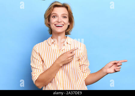 Positive Frau zeigt mit zwei Fingern beiseite, bis Portrait schließen, sehen Sie hier, Kopie soace, Spitze für Anzeige Stockfoto