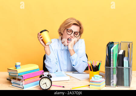 Müde Young Business woman holding Takeaway Kaffee Becher isoliert gelben Hintergrund, Studio geschossen, bis Portrait schließen, Müdigkeit Stockfoto