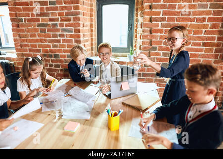 Junge erfolgreiche Business Kinder ihren Sieg feiern, Mädchen in Gläser mit pferdeschwänze Holding ein Glas Wasser, einen Toast vor ihr Stockfoto