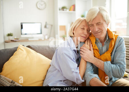 Portrait der liebevollen Umarmung senior Paar zärtlich auf bequemen Couch zu Hause sitzen, kopieren Raum Stockfoto