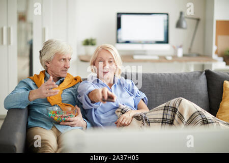 Portrait des modernen Senior paar TV zusammen beobachten, auf frustrierte Ehemann an Frau Schaltkanäle, kopieren Raum Suche Fokus Stockfoto