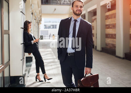 Gerne ambitionierter Geschäftsmann aus dem Bürogebäude, elegante Frau im eleganten Anzug mit einer Tablette lehnte sich an die Wand. nach oben schließen Foto Stockfoto