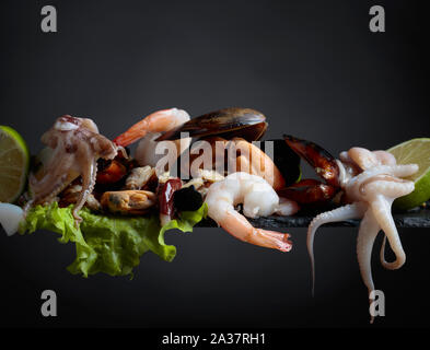 Köstliche Meeresfrüchte mit Salat und Kalk Schichten auf einem schwarzen Hintergrund gemischt. Stockfoto