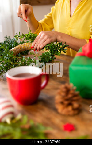 7/8 shot der jungen Frau, die einen Kranz nieder. DIY Weihnachten Dekoration Konzept. Die Hände schließen bis 7/8 geschossen. Stockfoto