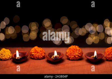 Diwali diya oder Ton öl Lampe brennende oder glühende auf einer hölzernen Oberfläche mit Ringelblume Blumen und Bokeh im Hintergrund und Kopieren eingerichtet. Konzept fo Stockfoto