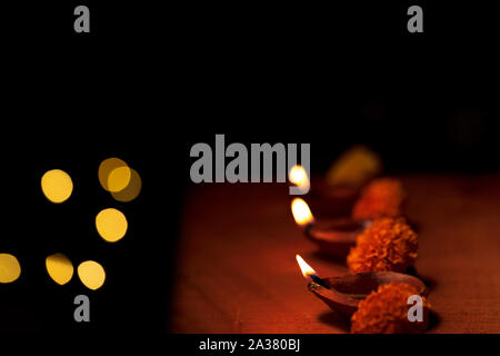 Diwali diya oder Terracotta Öllampen in eine Zeile oder eine Zeile mit Blumen und Kopieren in schwarzem Hintergrund und bokeh Lichter isoliert eingerichtet. Konzept für Stockfoto