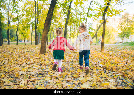 Zwei kleine Mädchen Freundinnen spielen im Herbst City Park halten sich an den Händen Stockfoto