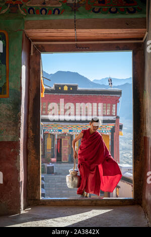 Ein junger Mönch gehen durch eine Tür an der Thiksey Kloster, Ladakh, Jammu und Kaschmir, Indien Stockfoto