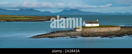 Einem stimmungsvollen Sonnenuntergang an der historischen St Cwyfan Kirche, Anglesey, befindet sich auf der kleinen Insel Gezeiten an der Küste von Cribinau - "Kirche am Meer" Stockfoto