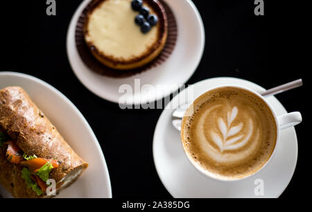 Frühstück mit Cappuccino mit Kaffee Kunst und Lachs Sandwich Stockfoto