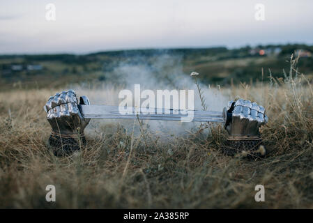 Metall Handschuhe und Schwert, das aus dem Boden Stockfoto