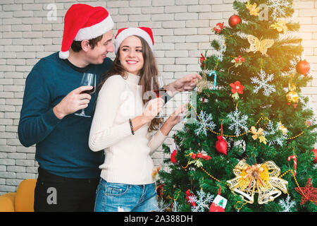 Feier der Weihnacht von Paaren. Junge Menschen sind, die ihre Freundinnen, mit einem Glas Wein und genießen stehen neben dem Weihnachten Stockfoto