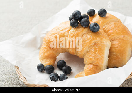 Croissants mit frischen Blaubeeren im Korb liegt leckeres Gebäck auf dem Tisch. Stockfoto