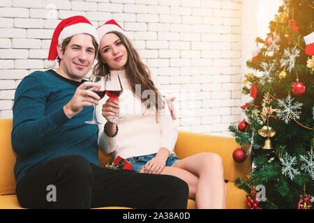 Europäische Paare, kaukasischer Mann mit blauen Pullover und Frau tragen weiße Pullover, Mütze tragen, Sitzen, trinken Rotwein in Weihnachten Meer Stockfoto