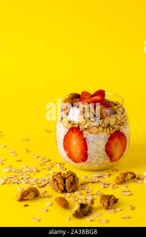 Chia Pudding mit Erdbeeren, oatmeals und Nüsse in einem Glas auf gelben Hintergrund. Detox und gesunden superfoods Frühstück Konzept. Stockfoto