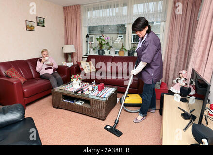 Ein Betreuer Staubsauger das Wohnzimmer der älteren Frau Stockfoto