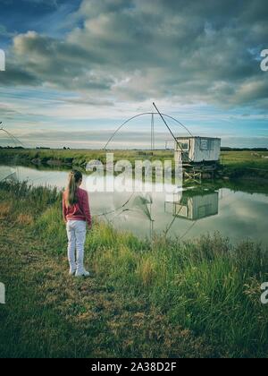 Stehendes Mädchen durch einen Fluss in Fischerhütten und Netze, Rue du Gois Causeway, Noimoutier Insel, Vendee, Frankreich Stockfoto