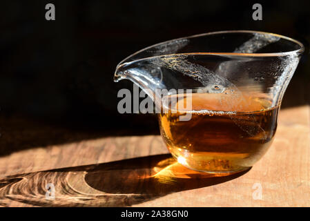 Nahaufnahme eines chinesischen Teekanne aus Glas mit schwarzen frischen Tee auf dem Tisch zu stehen gegen einen dunklen Hintergrund mit dem Sonnenlicht durch it Stockfoto