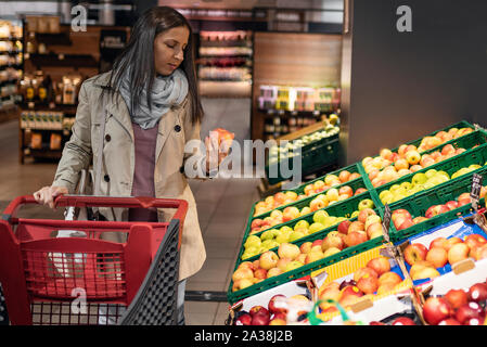 Hausfrauen, Frauen mit Warenkorb im Supermarkt. Wunderschöne junge Frau mit einem Warenkorb Blick auf einige Produkte auf einen Supermarkt in Gang. Frau Stockfoto