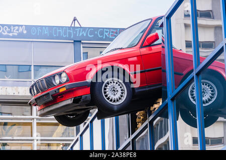 Ein rotes BMW Auto hängt, die prekär aus dem Dach eines Gebäudes, wie wenn es nur als Folge eines Unfalls, Rotterdam, Niederlande gebrochen hatte. Stockfoto
