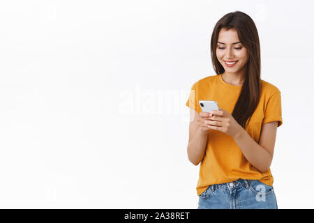 Fröhlich, freundlich - auf der Suche feminine Frau im gelben T-Shirt Messaging, lächeln, glücklich und zufrieden, Browsen mit dem Smartphone internet, schwarz Einkaufen Stockfoto