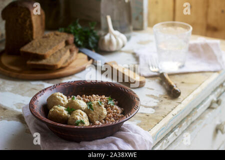 Fleischbällchen in saurer Sahne-Sauce, serviert mit Buchweizenbrei, Brot und Knoblauch. Rustikaler Stil. Stockfoto