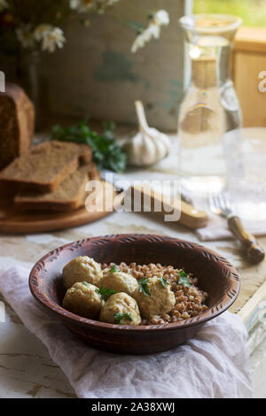 Fleischbällchen in saurer Sahne-Sauce, serviert mit Buchweizenbrei, Brot und Knoblauch. Rustikaler Stil. Stockfoto