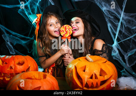 Mutter und ihrer Tochter in Hexe Kostüme Halloween Feiern mit Halloween Süßigkeiten und süße über Spider web Stockfoto