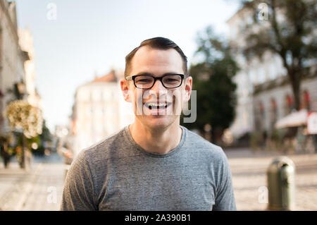 Die Hälfte Körper geschossen des jungen Mannes in einer Straße, einer alten Stadt in Europa, die in der Kamera mit braunen Augen und eyesglasses Stockfoto