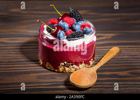 Frühstück mit Müsli, frischem Obst und Joghurt auf einem dunklen Holztisch Stockfoto