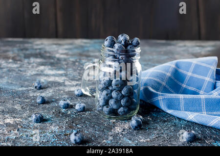 Reifen Heidelbeeren im Glas Glas mit Blätter Minze auf einem dunklen konkreten Hintergrund Stockfoto