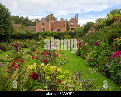 Chenies Manor versunkenen Garten auf einem September abends in Richtung des Tudor House schauen durch die Anpflanzung von farbenfrohen Dahlien, Pfad und Gitter. Stockfoto